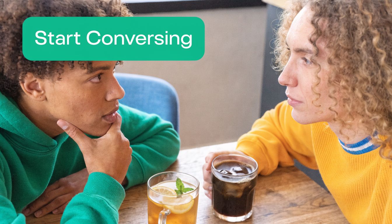 Two young people with curly hair having a serious conversation while drinking iced beverages at a cafe.