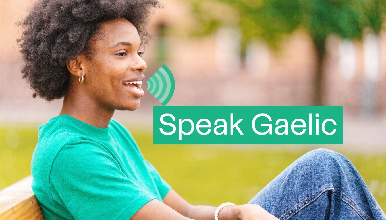 A person with curly hair wearing a green shirt smiling with a Speak Gaelic graphic overlay.