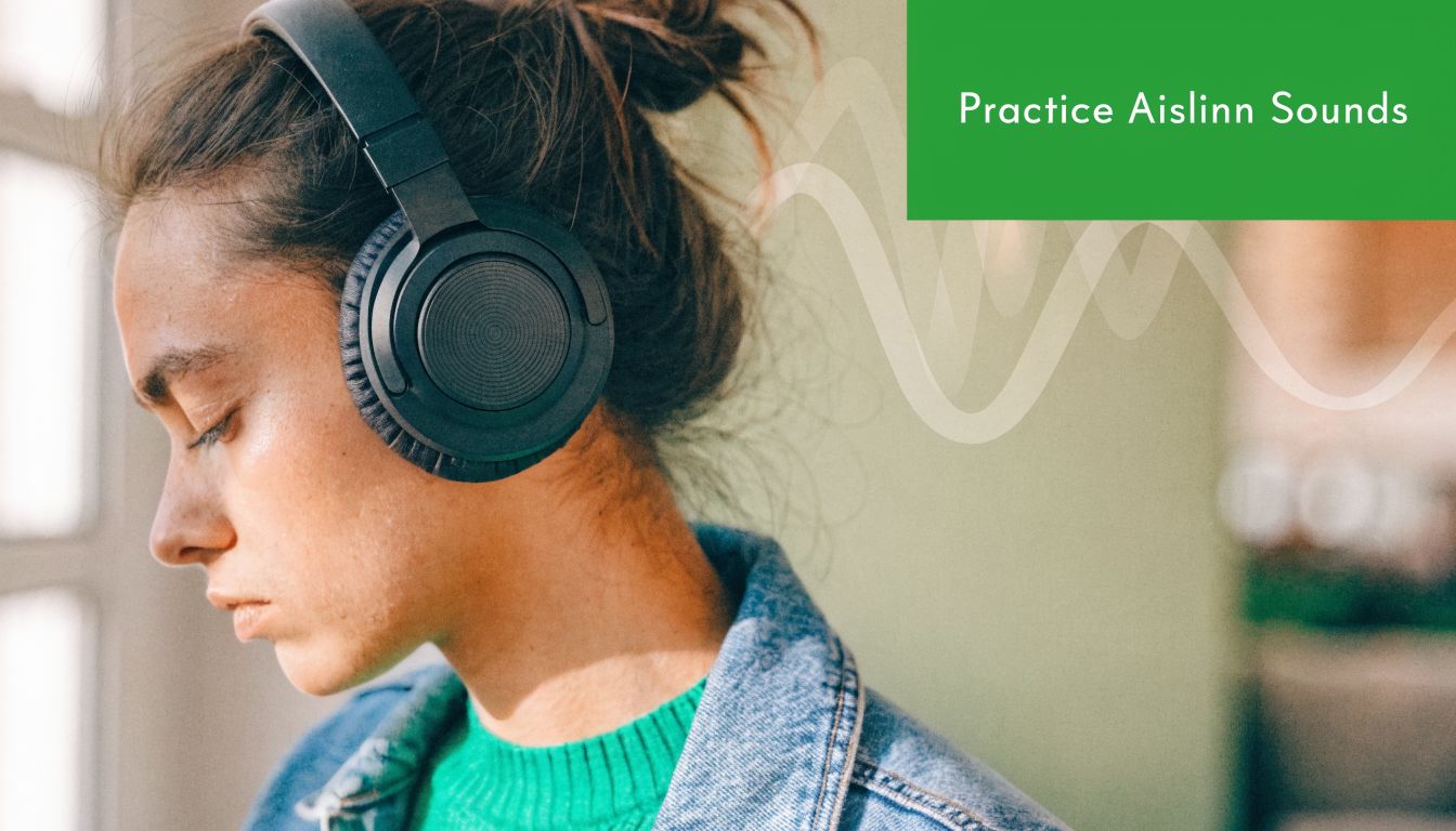 A young woman wearing headphones, focusing on listening during her pronunciation practice of the name Aislinn.