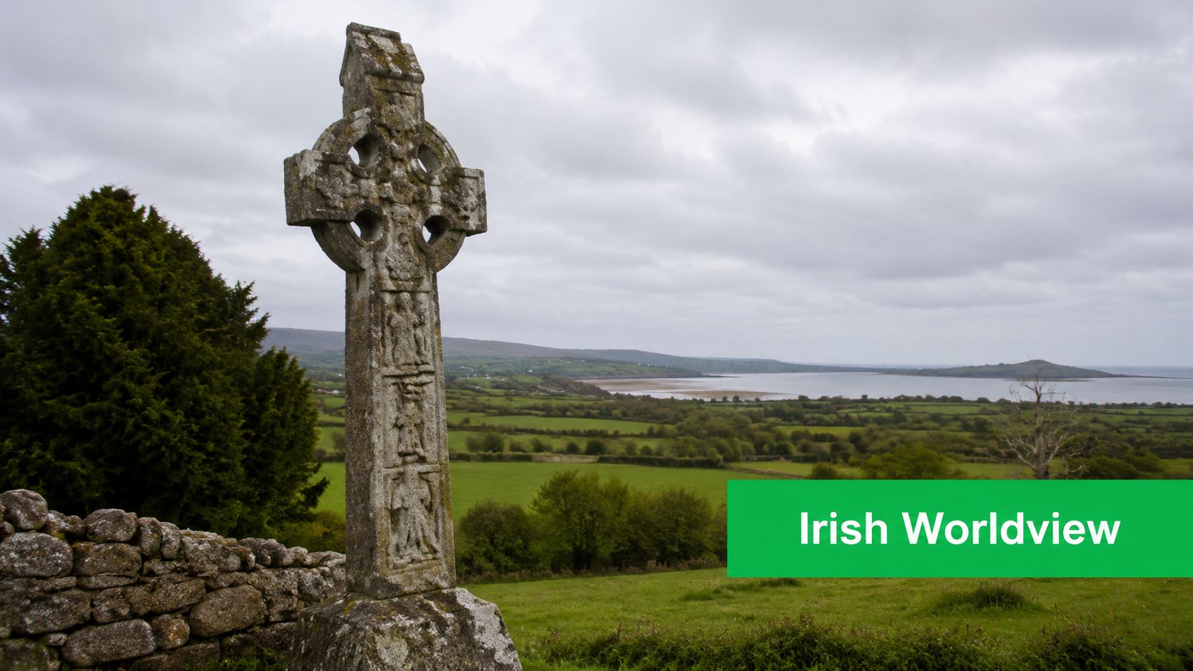 A historic stone Celtic cross standing in a lush green Irish landscape overlooking a coastal bay.