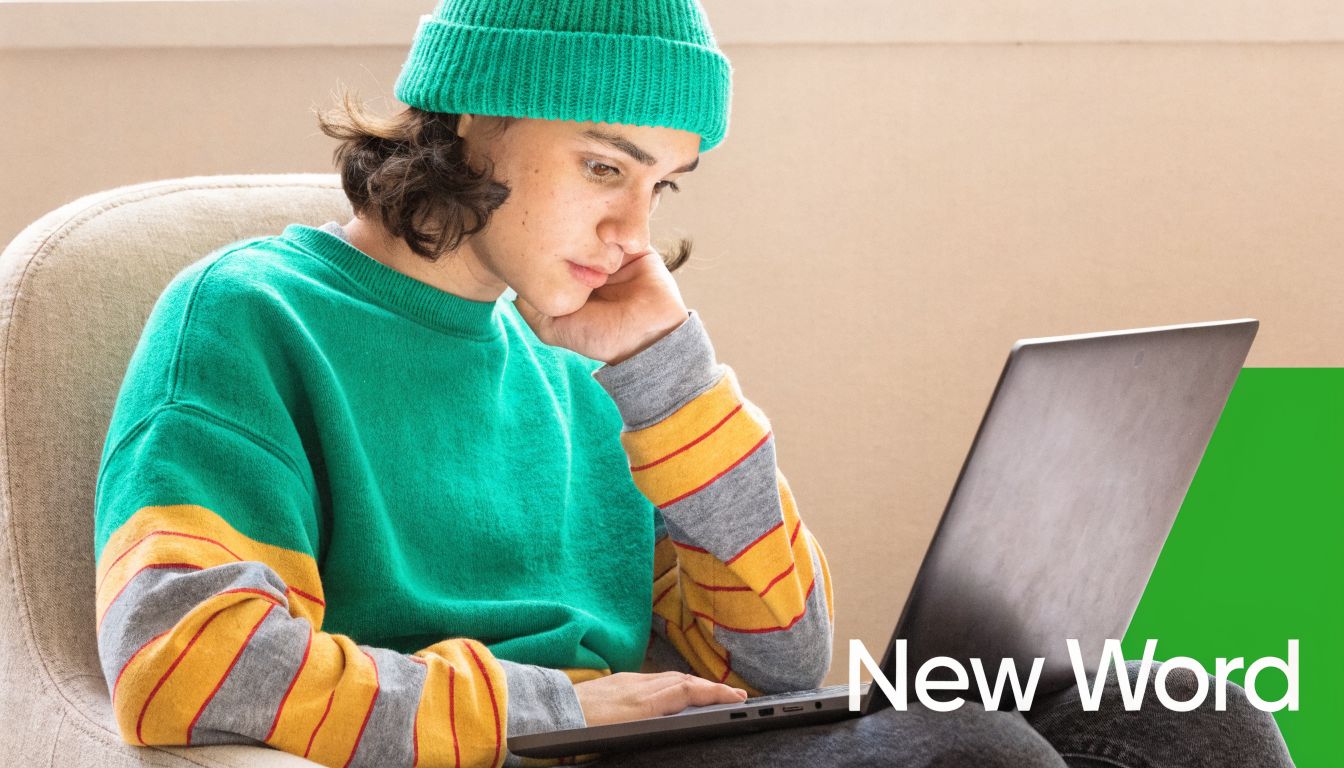 A person in a green beanie and sweater typing on a laptop while sitting in a chair.